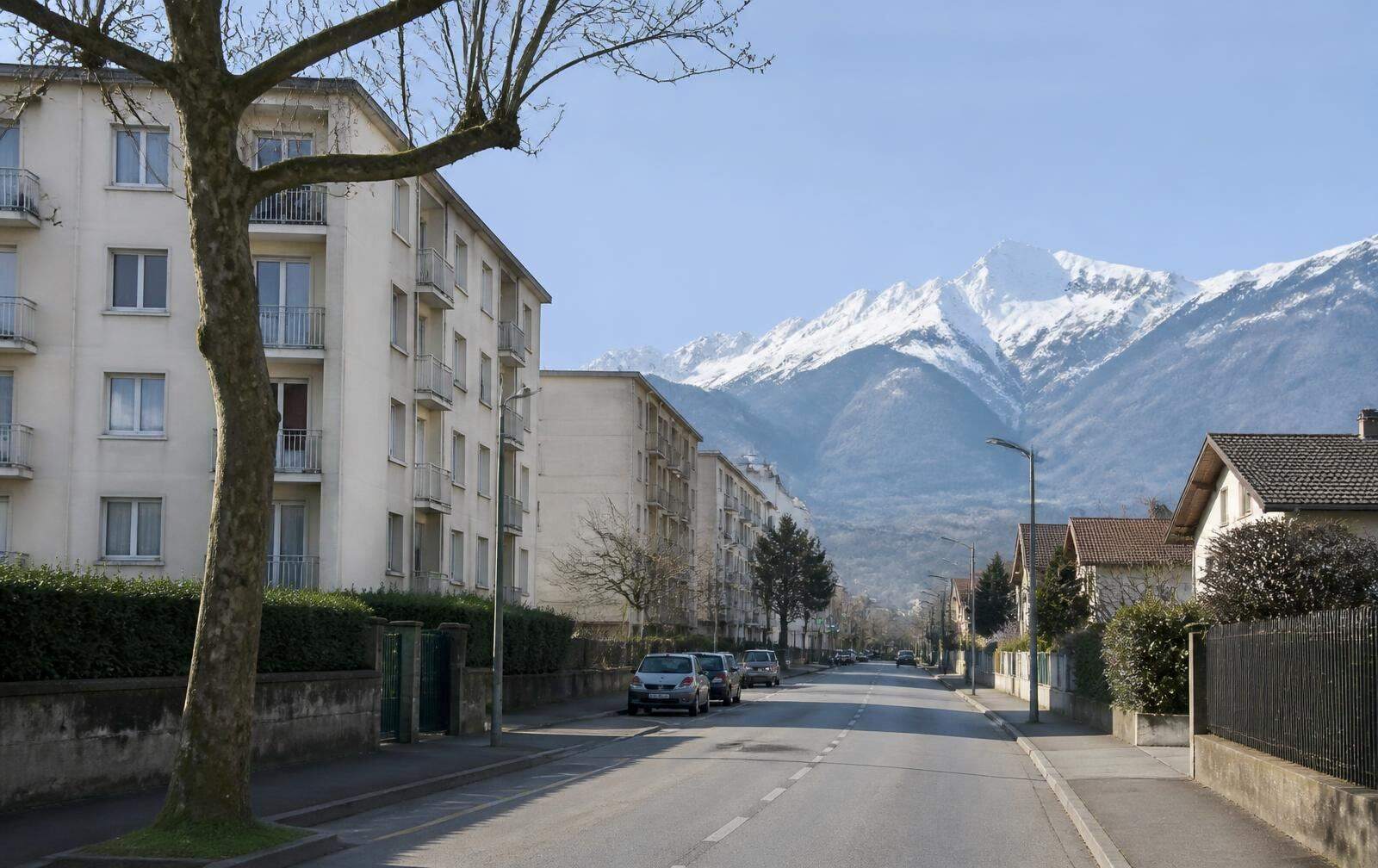 Rue résidentielle du sud de l'agglomération grenobloise, immeubles bas et sommets enneigés à l'horizon.